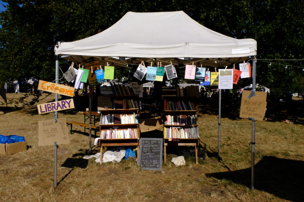 The photo shows a booth at the System Change Camp where activists can borrow books to read.