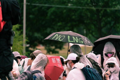 Aktivist*innen laufen mit Schirmen, auf einem Schirm steht "No LNG"