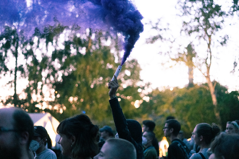 Eine Menschengruppe läuft, eine Person hält eine violette Rauchbombe in die Luft.