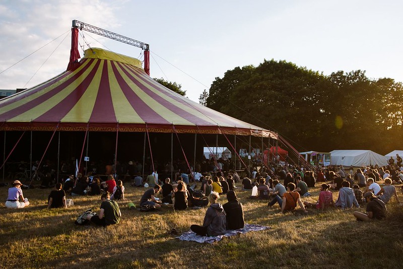 People sitting around a circus tent on the lawn in the sun.