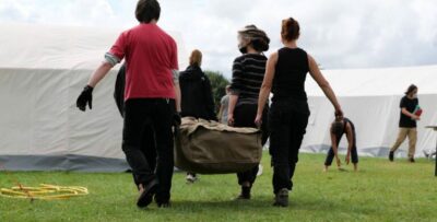Campaufbau: 4 Menschen tragen gemeinsam Zeltmaterial, im Hintergrund stehen bereits aufgebauate Zelte