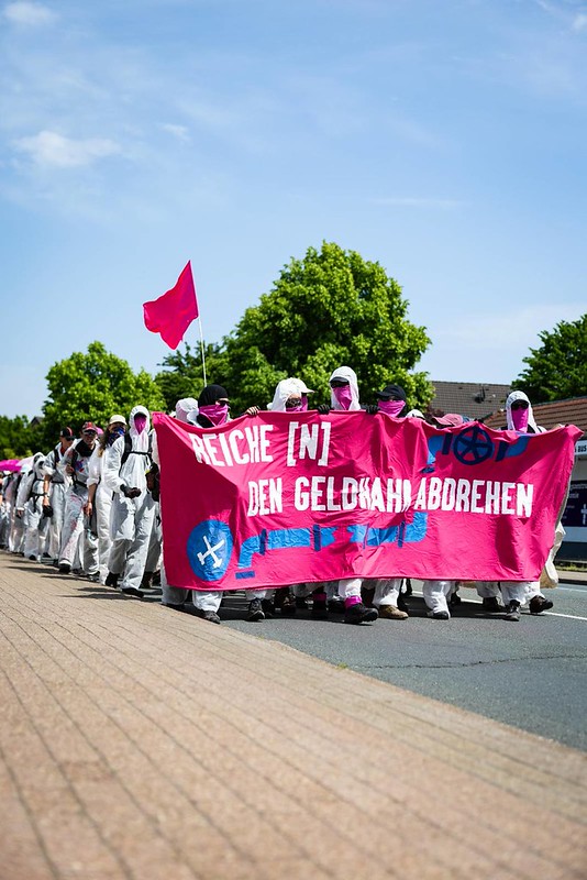 Ein Demoblock aus Menschen in weißen Maleranzügen. Auf dem Fronttranspi steht "Reiche (n) den Geldhahn abdrehen"