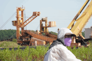 industrial infrastructure behind a sitting masked activist. (c) Revolution archived.