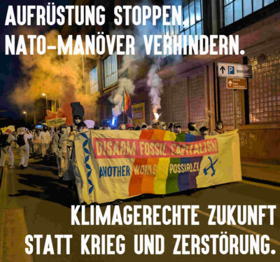 Foto vom bunten Finger auf dem Weg zur Aktion. Überschrieben mit Aufrüstung stoppen, NATO-Manöver verhindern. Klimagerechte Zukunft statt Krieg und Zerstörung.