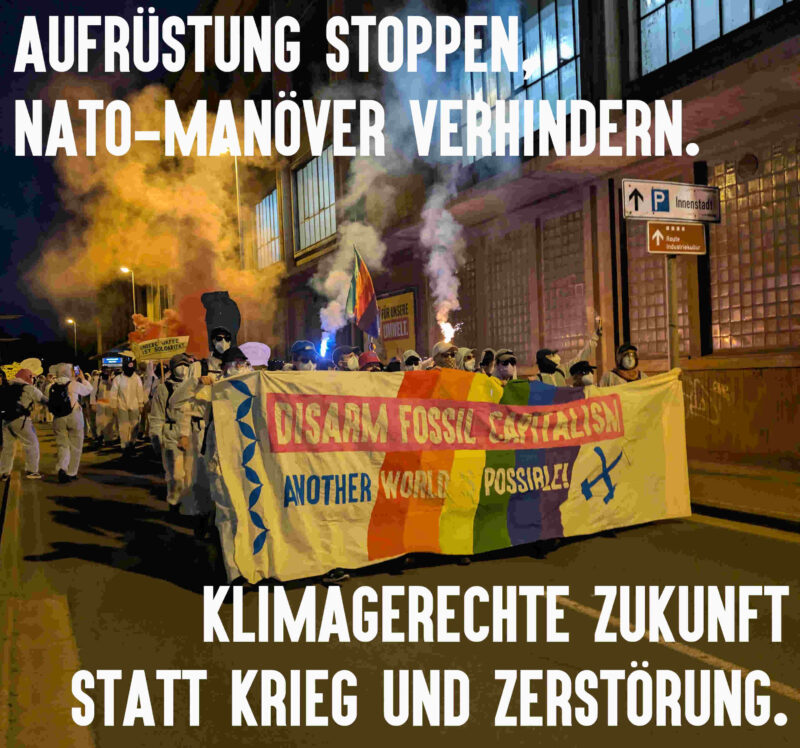 Foto vom bunten Finger auf dem Weg zur Aktion. Überschrieben mit Aufrüstung stoppen, NATO-Manöver verhindern. Klimagerechte Zukunft statt Krieg und Zerstörung.